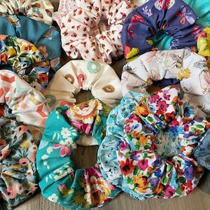 May include: A collection of fabric hair scrunchies featuring various patterns including floral prints, butterflies, bees, cacti, donuts, and geometric shapes in a wide array of colors such as teal, yellow, pink, blue, white, and green.