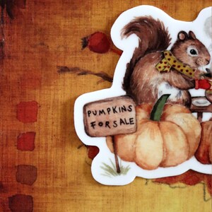 May include: A watercolor illustration of a squirrel selling pumpkins. The squirrel is wearing a yellow and red polka dot scarf and holding a sign that says "Pumpkins for Sale".