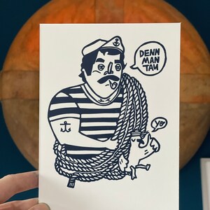 Könnte beinhalten: Eine blaue und weiße Illustration eines Seemanns mit einem Seil um seinen Körper. Der Seemann trägt ein gestreiftes Hemd, einen Hut mit Anker und einen Schnurrbart. Der Seemann sagt "DENN MAN TAU".