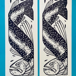 Könnte beinhalten: Zwei vertikale Kunstdrucke mit einem stilisierten schwarz-weißen Fischdesign. Der Fisch ist in einer geschwungenen Pose mit detaillierten Flossen und Schuppen dargestellt. Die Drucke befinden sich auf weißem Papier vor blauem Hintergrund.