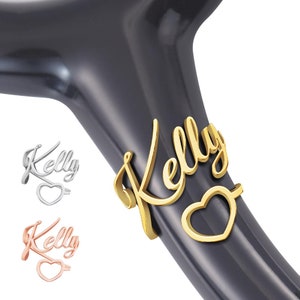 May include: Gold-colored stethoscope charm with the name "Kelly" and a heart. The charm is attached to a black stethoscope.