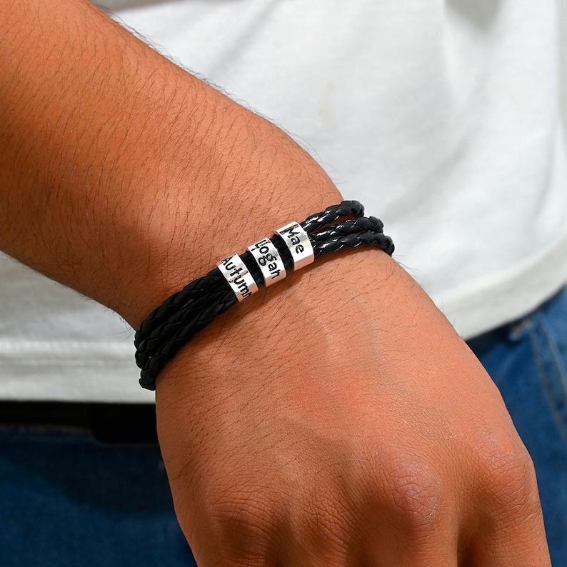 May include: Black leather bracelet with three silver beads engraved with the names "Autumn", "Logan", and "Mae".