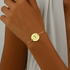 May include: Gold bracelet with a round charm featuring a medical symbol, the Star of Life.