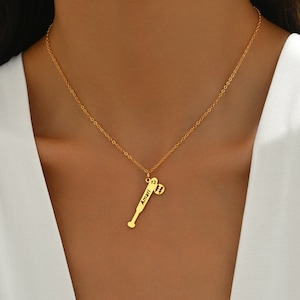 May include: Gold necklace featuring a baseball bat pendant. The bat is engraved with the name "Amari" and the number "13". A small baseball charm dangles from the bat.