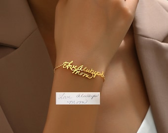 May include: A gold bracelet featuring the cursive inscription "Love always mom". The bracelet is attached to a fine chain. A handwritten note with the same text is visible below the bracelet.