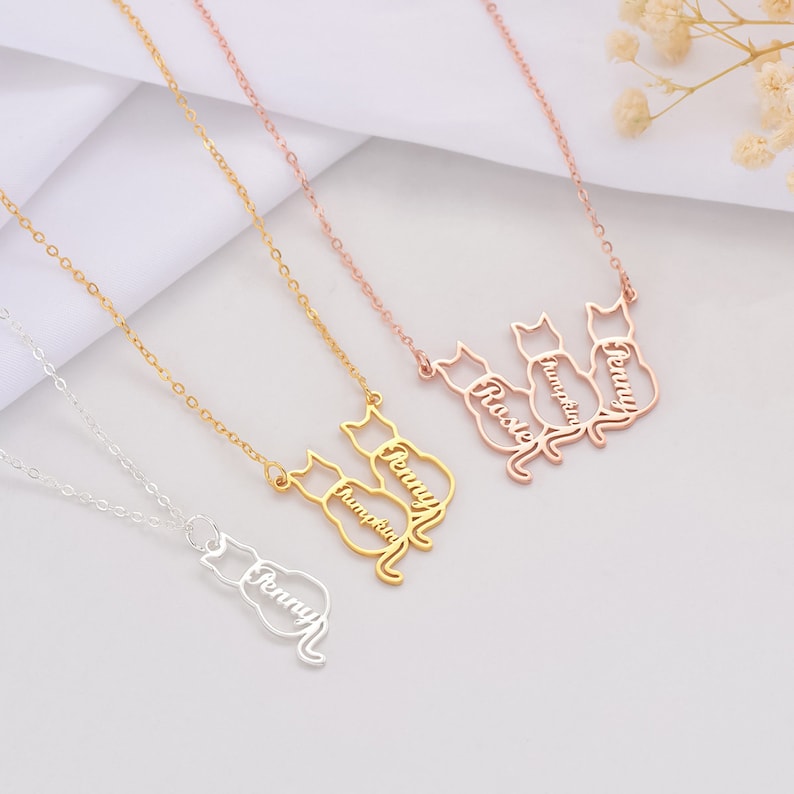May include: Three gold cat necklaces with the names Penny,  Humphrey, and Rosie. The necklaces are on a white background.
