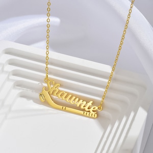 May include: Gold necklace featuring the name "Shawnté" and a hockey stick pendant.