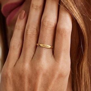 Könnte beinhalten: Ein polierter goldfarbener Bandring mit einem flachen, horizontalen Steg auf der Vorderseite. In die Mitte des Stegs ist der Name Sophia in einer kursiven Schrift eingraviert. Der Ring hat eine glatte, metallische Oberfläche und eine schlichte Form.
