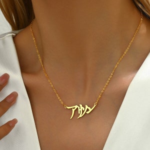 Pode incluir: Um colar de corrente de ouro com um pingente que apresenta a palavra japonesa "Anya" em escrita estilizada.