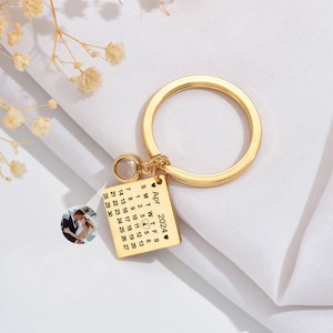 May include: Gold keychain with a small photo of a couple, a clear crystal charm, and a calendar engraved with the date "April 2024".