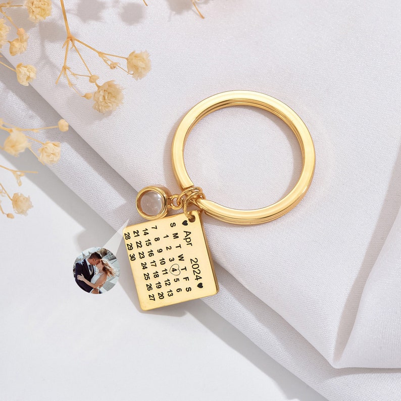 May include: Gold keychain with a small photo of a couple, a clear crystal charm, and a calendar engraved with the date "April 2024".