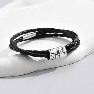 May include: Black leather bracelet with a silver charm featuring the names "Mae", "Logan", and "Autumn".