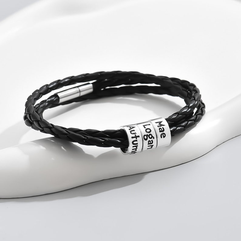 May include: Black leather bracelet with a silver charm featuring the names "Mae", "Logan", and "Autumn".