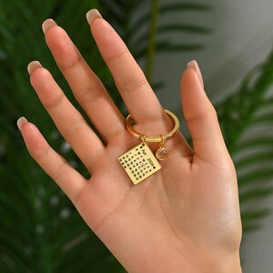 May include: Gold keychain with a square charm featuring a calendar for April 2024. The charm has a small, clear crystal attached to it.