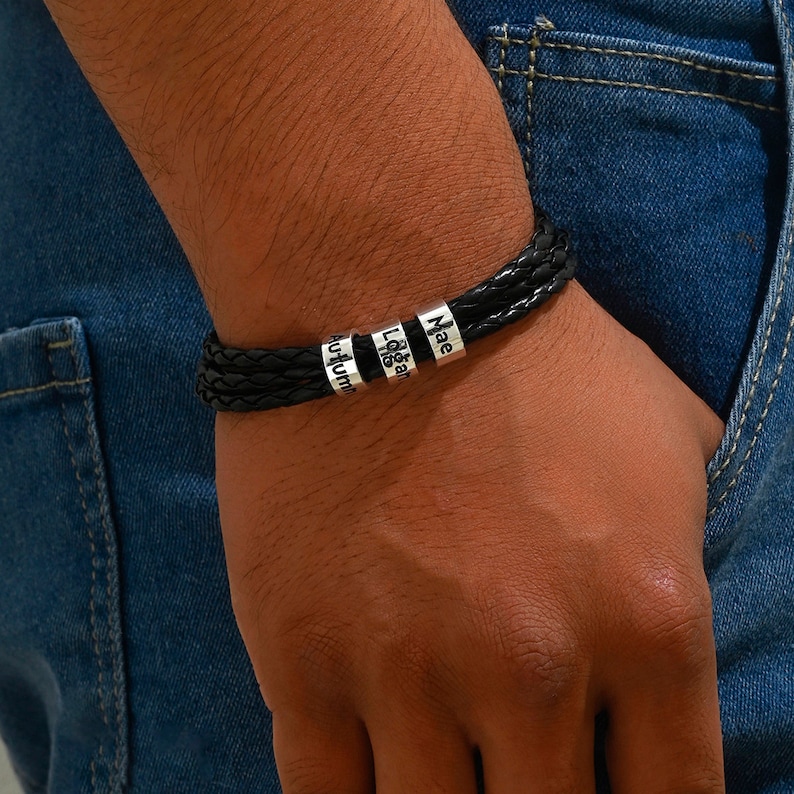 May include: Black leather bracelet with silver beads engraved with the names "Mae", "Logan", and "Autumn".