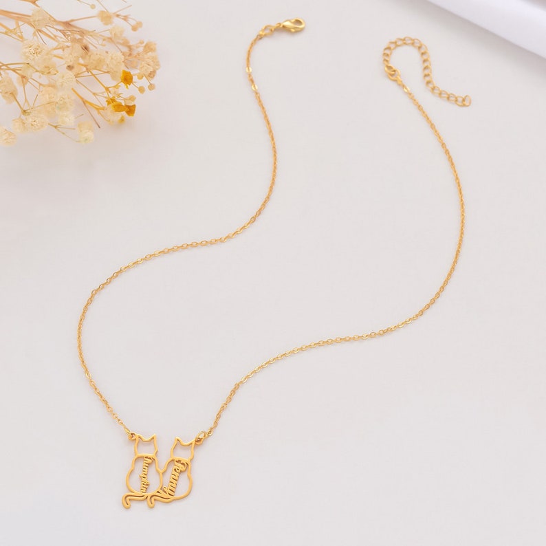 May include: Gold necklace with two cat silhouettes, each with a name inscribed inside. The names are "Vanessa" and "Tommy".