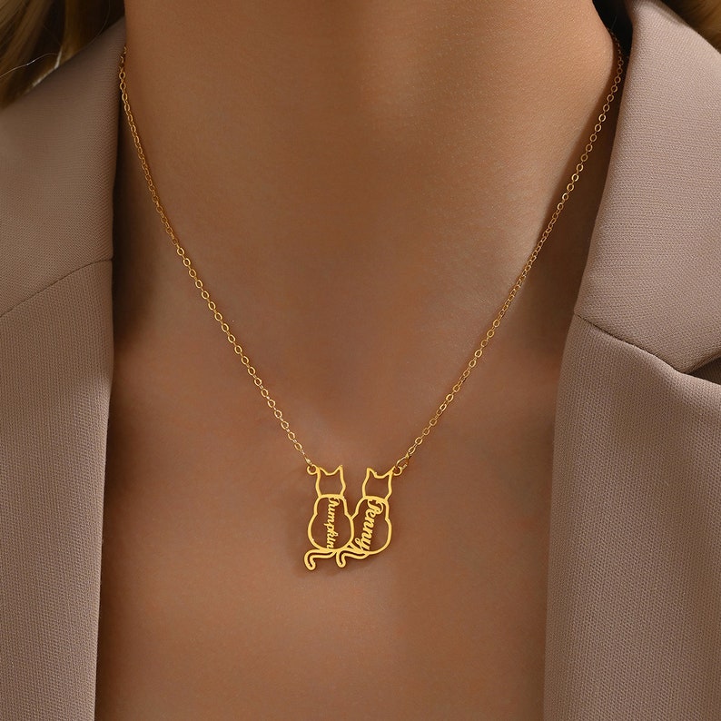 May include: Gold necklace with two cat silhouettes, each with a name inscribed on the back. The names are "Pumpkin" and "Penny".