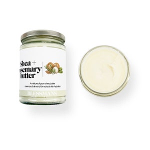 May include: A glass jar of shea and rosemary butter with a white label that reads "Shea + Rosemary Butter" and "A mixture of pure shea butter, rosemary & almond for natural skin hydration." The label also includes a small illustration of shea nuts, rosemary sprigs, and almonds. The jar is sitting on a white background.