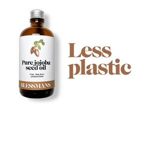 May include: A brown glass bottle with a silver lid and a white label that reads "Pure jojoba seed oil" and "Blessmans". The bottle is sitting on a white background with the text "Less plastic" in brown letters.