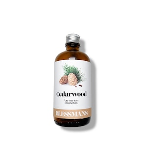May include: A brown glass bottle with a silver cap, labeled "Cedarwood." The label features illustrations of pine cones and needles. The text "Pure-free from preservatives" and the brand name "BLESSMANS" are also visible.
