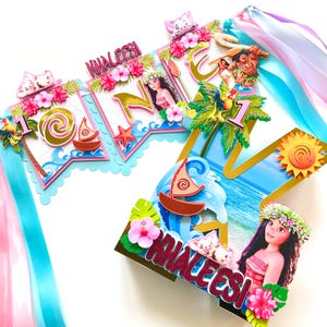 May include: A colorful banner with the name "Khaleesi" and the number "1" featuring images of Moana characters, palm trees, and sailboats. The banner is decorated with pink and white flowers and blue and pink ribbons.