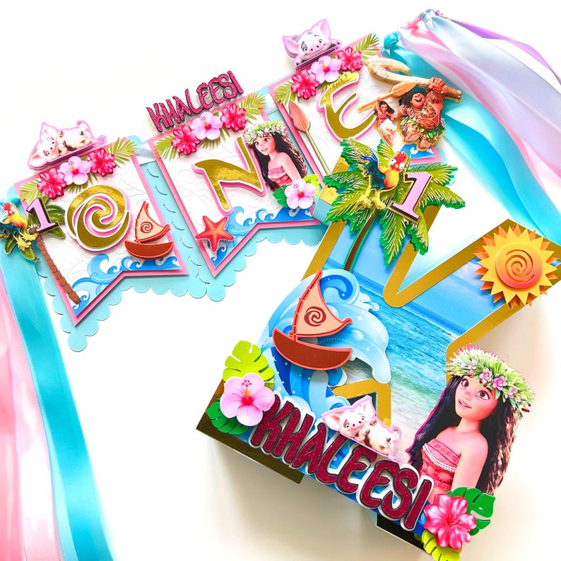 May include: A colorful banner with the name "Khaleesi" and the number "1" featuring images of Moana characters, palm trees, and sailboats. The banner is decorated with pink and white flowers and blue and pink ribbons.