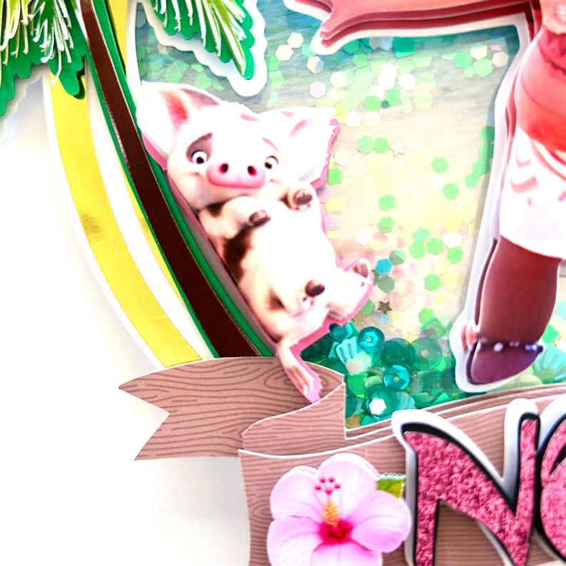 May include: A 3D cake topper featuring a pig from the movie Moana. The pig is pink with brown spots and is hanging upside down. The topper also includes a palm tree, a green and blue glitter background, and a pink hibiscus flower. The text "Noa" is written in pink glitter.