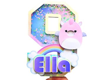 Puede incluir: Un adorno para pastel colorido con un unicornio rosa, un arcoíris y nubes. El número 8 está en el fondo con purpurina y una ventana. El nombre "Ella" está escrito en letras moradas.