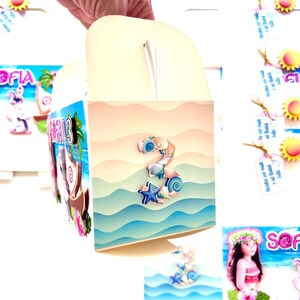 May include: A cream-colored party favor box with a handle, decorated with a beach-themed design. The box features a large number "3" made of seashells and a blue starfish. The background depicts ocean waves and a sandy beach.