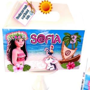 May include: A white gift box with a handle, decorated with a tropical theme. The box features the name "Sofia" in pink, a cartoon character, a boat, and a number "3". A tag with text is attached.