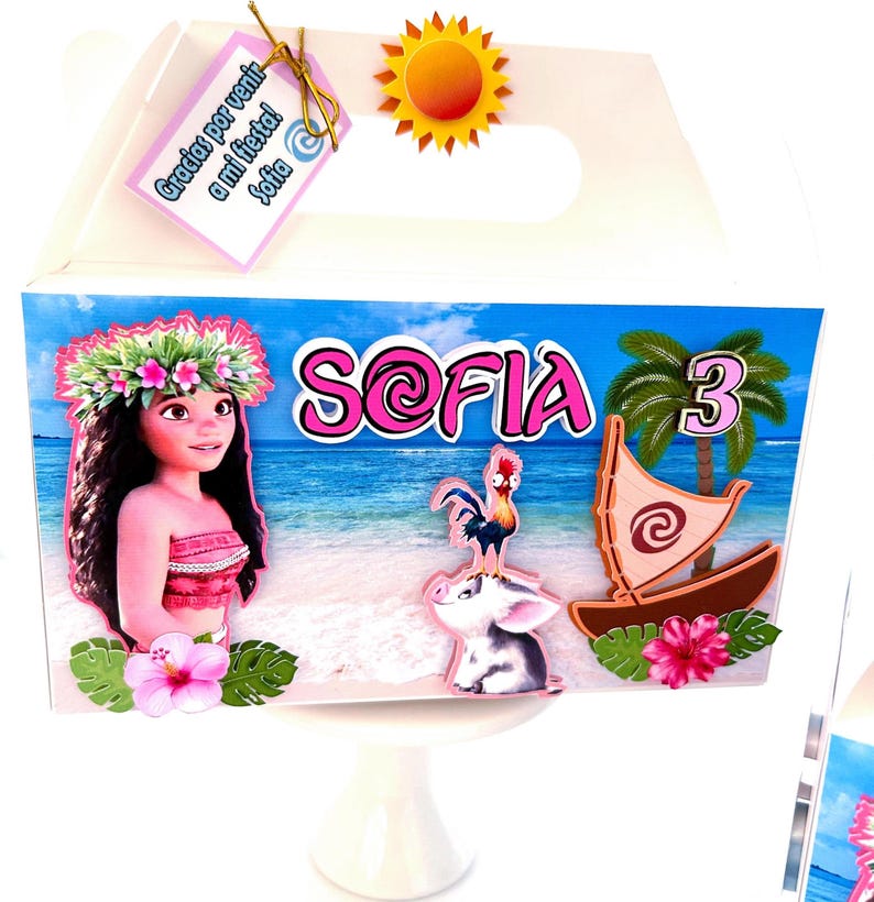 May include: A white gift box with a handle, decorated with a tropical theme. The box features the name "Sofia" in pink, a cartoon character, a boat, and a number "3". A tag with text is attached.