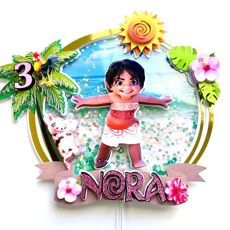 May include: A pink and gold cake topper featuring a cartoon character from the movie Moana. The character is standing on a beach with a pig and a palm tree. The cake topper also includes a pink banner with the name "Nora" and the number "3".