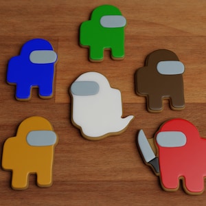 May include: Six colorful cookies shaped like characters from the video game Among Us. The cookies are on a wooden surface. One cookie is white and shaped like a ghost.