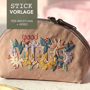 Könnte beinhalten: Eine rosa Canvas-Kosmetiktasche mit dem Schriftzug "good vibes", der in bunten Fäden gestickt ist. Die Tasche ist mit gestickten Blumen verziert.