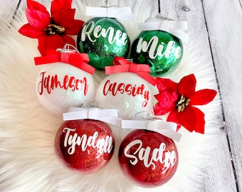 Könnte beinhalten: Sechs personalisierte Weihnachtskugeln mit Glitzer. Die Kugeln sind rot, weiß und grün. Die Namen auf den Kugeln sind Renee, Mike, Jameson, Cassidy, Tyndall und Sadie.