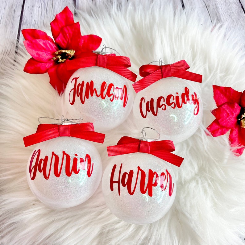 May include: Four white, glittery Christmas ornaments with red bows and personalized names:  "Jameson", "Cassidy", "Harrin", and "Harper".