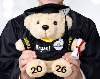 May include: A plush teddy bear wearing a graduation cap and gown. The bear has the name "Bryant" on its gown and the year "2026" on its foot. It also holds a miniature diploma. The bear is a graduation gift.