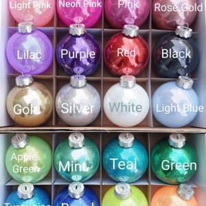 May include: A set of 18 round Christmas ornaments with glitter finishes in various colors, including light pink, neon pink, pink, rose gold, lilac, purple, red, black, gold, silver, white, light blue, apple green, mint, teal, green, turquoise, royal, yellow, and orange.