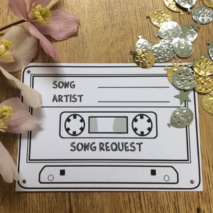 May include: A white cassette tape song request card with black lines. The card has the words "SONG" and "ARTIST" with blank lines underneath. The card also has the words "SONG REQUEST" in the centre.