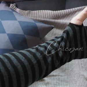 May include: Black and gray striped arm warmer with a thumb hole. The arm warmer is made of a soft, knitted fabric.
