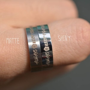 Może przedstawiać: Dwa srebrne pierścienie z napisem "Always Keep Fighting" na każdym pierścieniu. Pierścień po lewej stronie jest matowy, a pierścień po prawej stronie jest błyszczący.