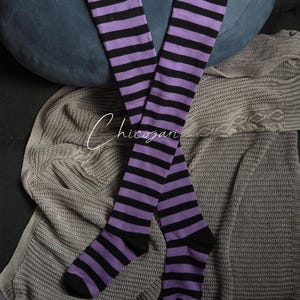 May include: A pair of black and purple striped thigh-high socks. The socks are made of a soft, stretchy material and are perfect for adding a pop of colour to any outfit.