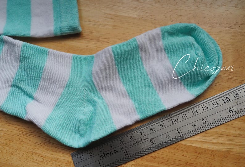 May include: A pair of white and turquoise striped socks. The socks are laid flat on a wooden surface with a ruler next to them.