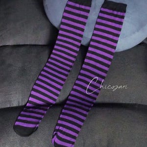 May include: A pair of purple and black striped knee-high socks. The socks are folded and laid out on a dark grey surface.