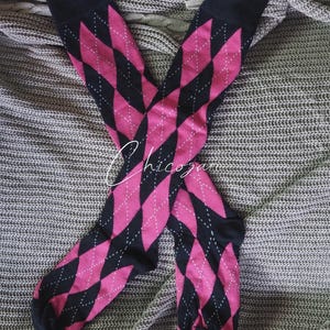 May include: Two pairs of knee-high socks with a pink and black argyle pattern. The socks have a black cuff, heel, and toe. The argyle pattern is made up of pink diamonds with white dotted accents.