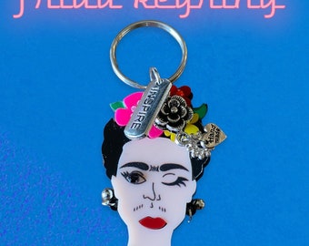 May include: A silver keyring featuring a colorful portrait of Frida Kahlo with the words "Inspire" and "Hand Made" on charms.