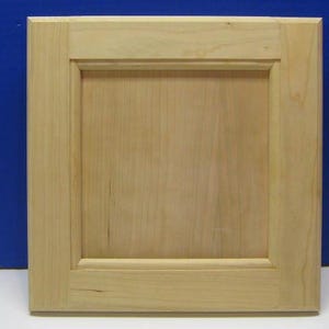 May include: A light-colored, square cabinet door with a recessed panel design. The door is made of wood and has a natural finish, showcasing the wood grain. The frame around the panel is slightly raised, adding dimension. The background is a solid blue.