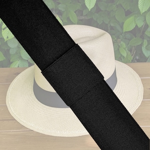 Könnte beinhalten: Ein schwarzes elastisches Hutband mit einem weißen Strohhut darunter. Das Hutband liegt auf einer Holzoberfläche.