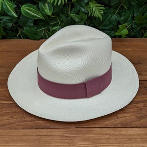 May include: A white Panama hat with a wide brim and a burgundy ribbon band.