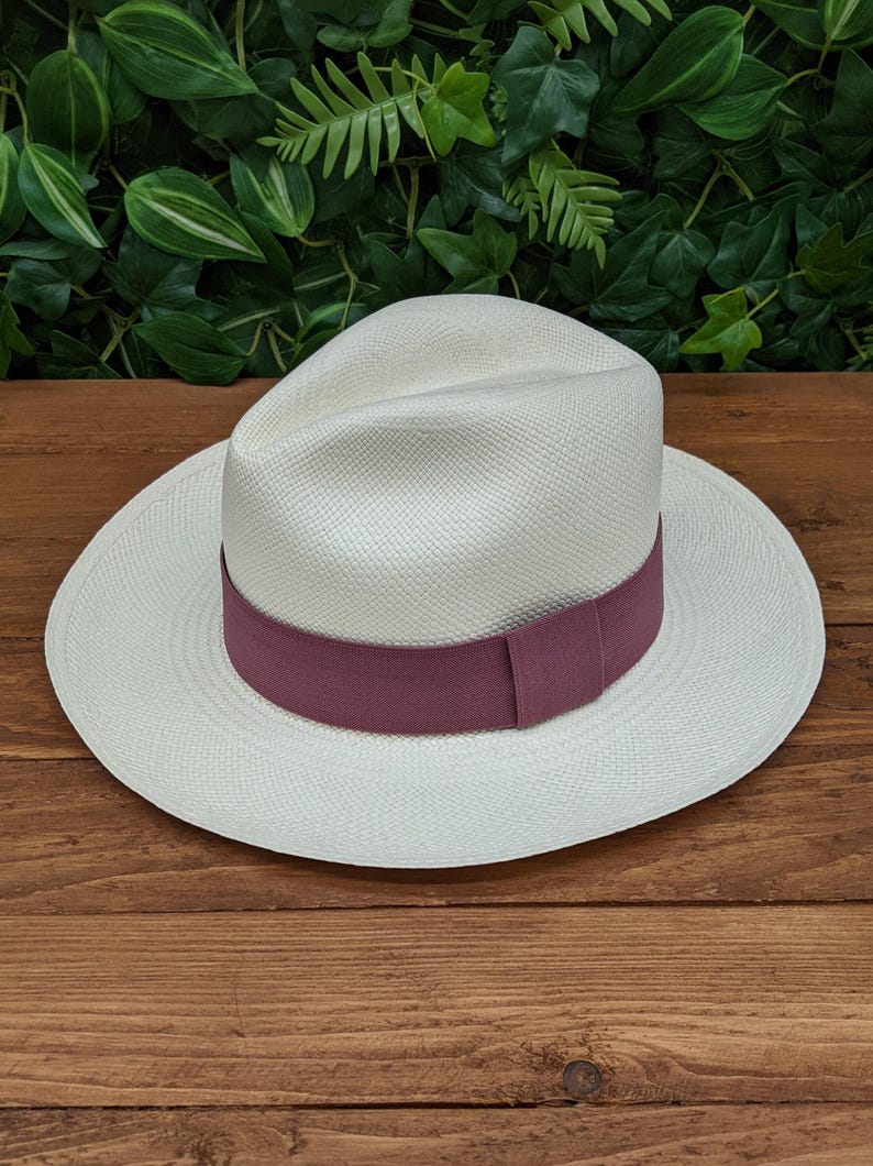 May include: A white Panama hat with a wide brim and a burgundy ribbon band.